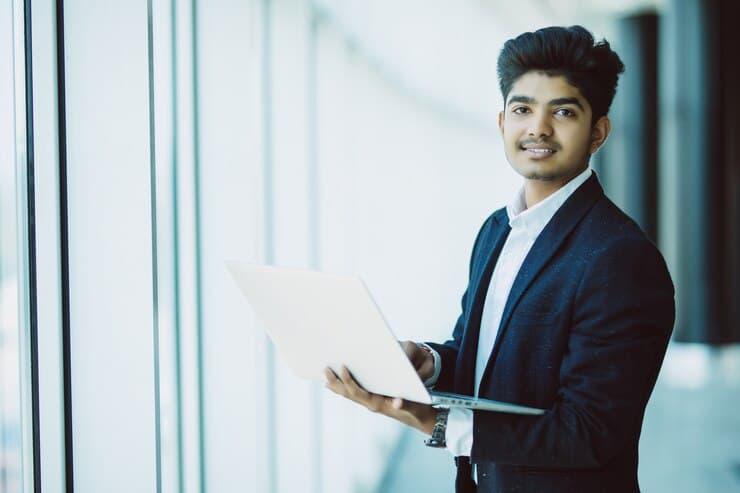 Young businessman holding a laptop in a bright office hallway